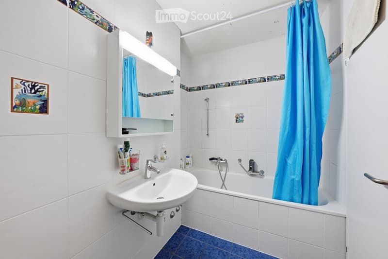 Bathroom with white tiles, blue floor, white sink, mirror, bathtub, blue shower curtain, towel rack