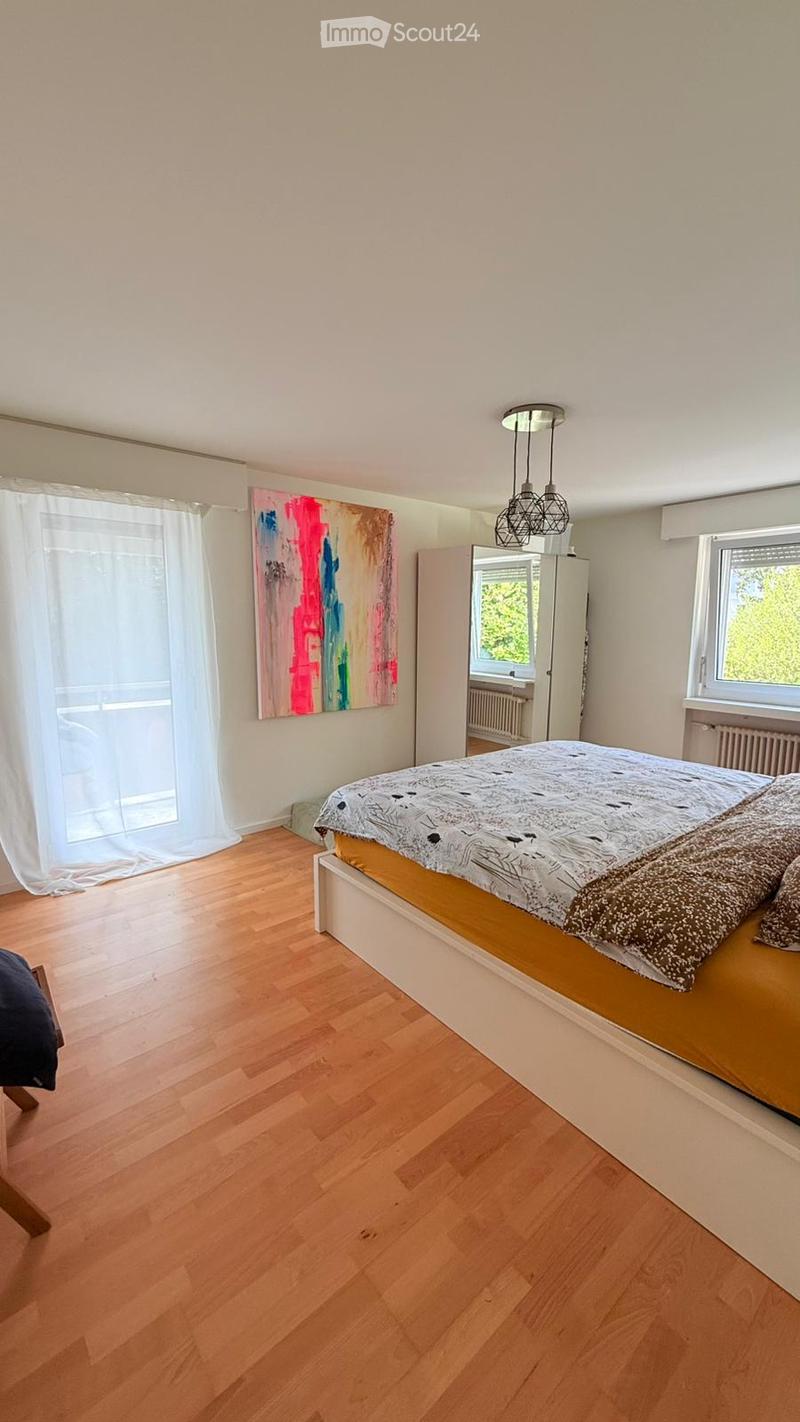 Bedroom with wooden floor, bed, white walls, white curtains, painting, mirror, radiator, ceiling lamp