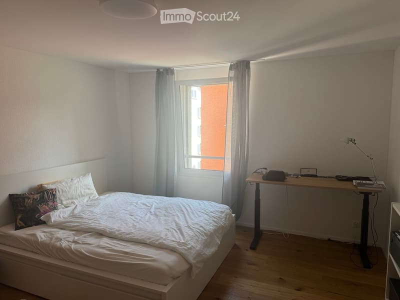 A bedroom with a bed, desk, lamp, and window with curtains.