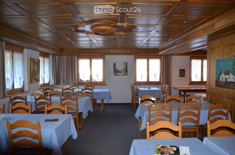 Dining room with wooden tables and chairs, wooden ceiling, windows with curtains, paintings on the wall