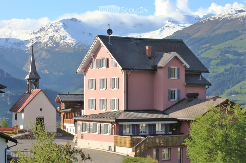 pink house, black roof, many windows, small church in the background, mountains in the background