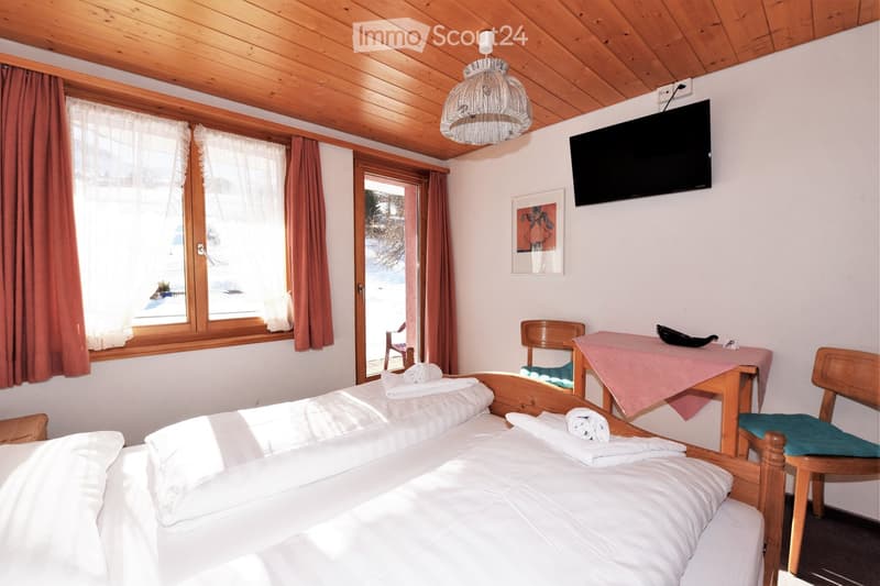 bedroom with two beds, wooden ceiling, white walls, large windows, TV, table, chairs, towels