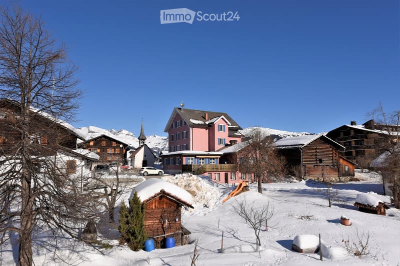 Snowy village with wooden houses, pink house in the center, mountains in the background