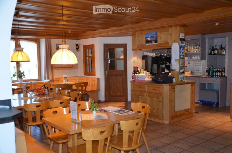 Wooden ceiling, wooden tables and chairs, wooden counter, shelves with bottles, lamps, plants, and a window with a view