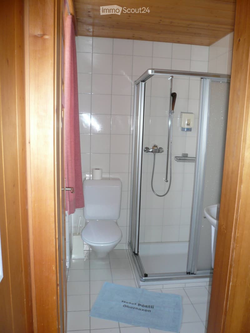 white tiled walls, white toilet, glass shower enclosure, white sink, towel, wooden door