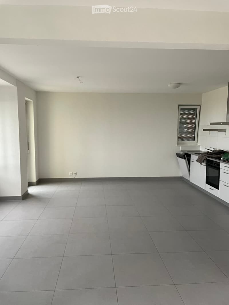 Empty room with white walls, gray tiles, power outlet, kitchen area with sink, dishwasher, and oven