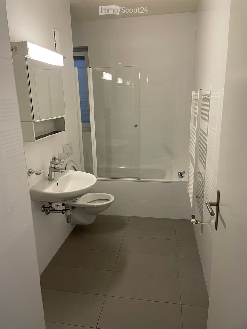 Bathroom with white tiles, white sink, white toilet, glass shower enclosure, white towel rack