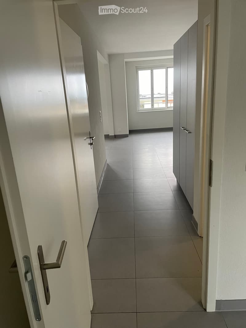 Empty hallway with white walls, gray tiles, and a window with a view outside.