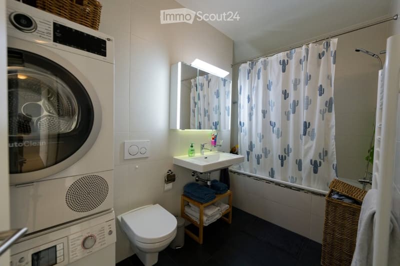 Bathroom with washing machine, sink, toilet, bathtub, shower curtain, towels, wicker basket, and wicker basket with towels.