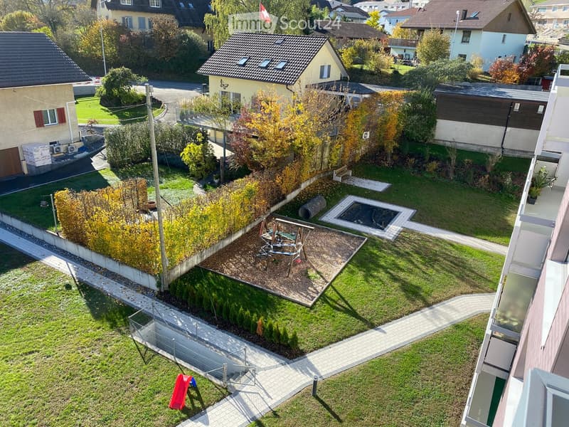 Aerial view of a garden with a playground, a small red slide, and a small pond.