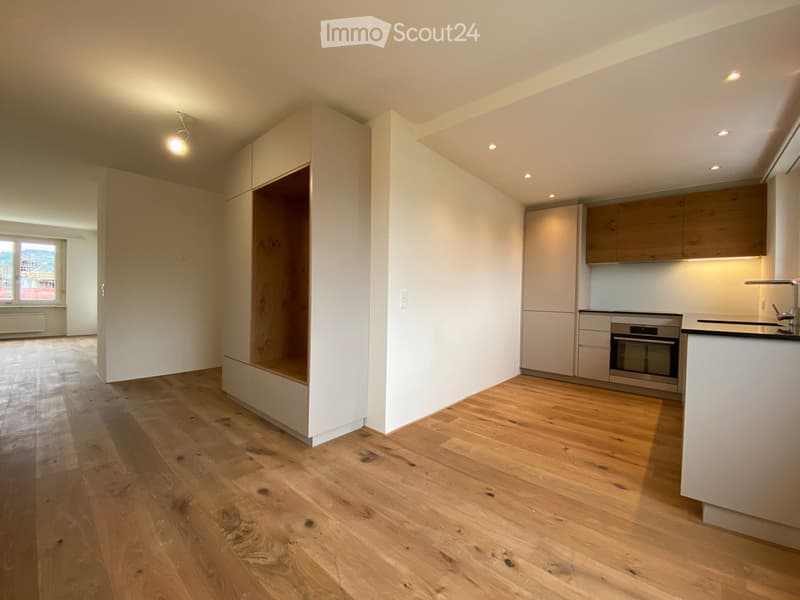 Empty room with wooden floor, white walls, built-in wardrobe, kitchen area with oven, sink, and cabinets