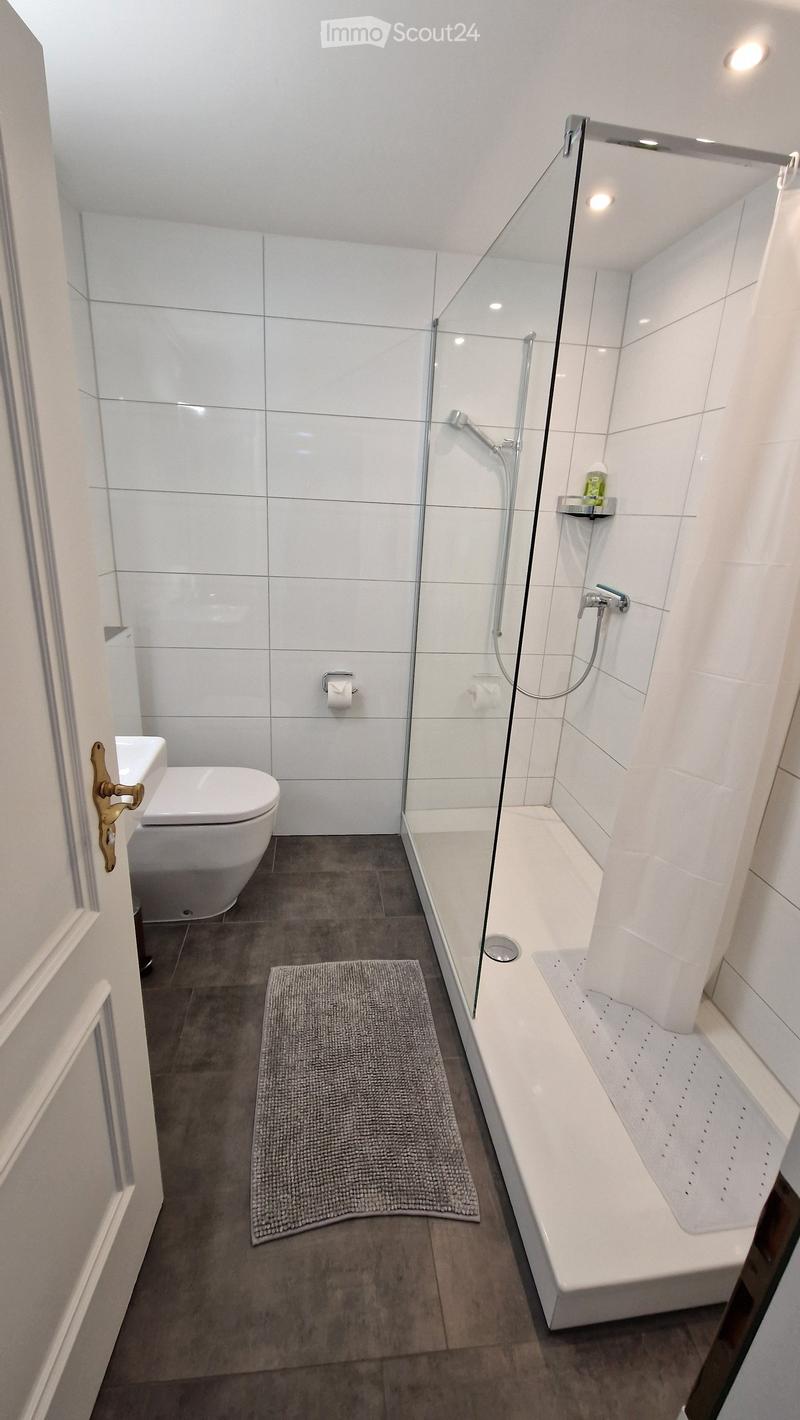 modern bathroom with white tiles, glass shower, white toilet, white sink, rug, shower curtain