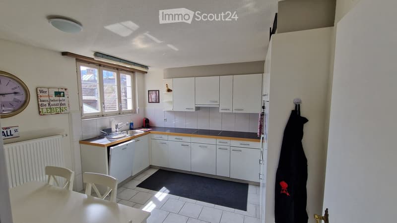 modern kitchen with white cabinets, black tiled floor, dishwasher, washing machine, window, radiator, clock, framed picture, black rug
