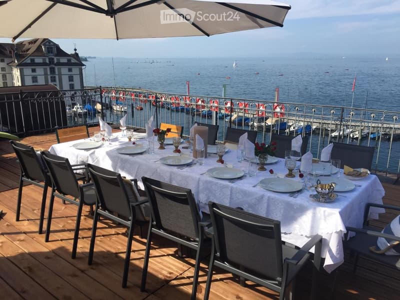 Dining table with chairs, white tablecloth, umbrella, view of the sea, boats docked
