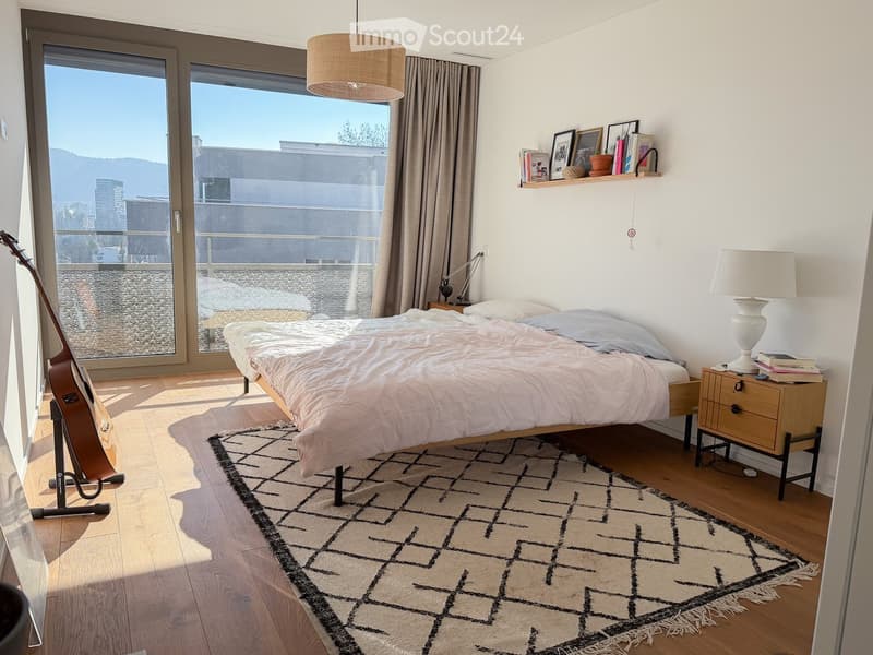 Bedroom with bed, rug, lamp, guitar, nightstand, and large glass doors leading to a balcony with a view.