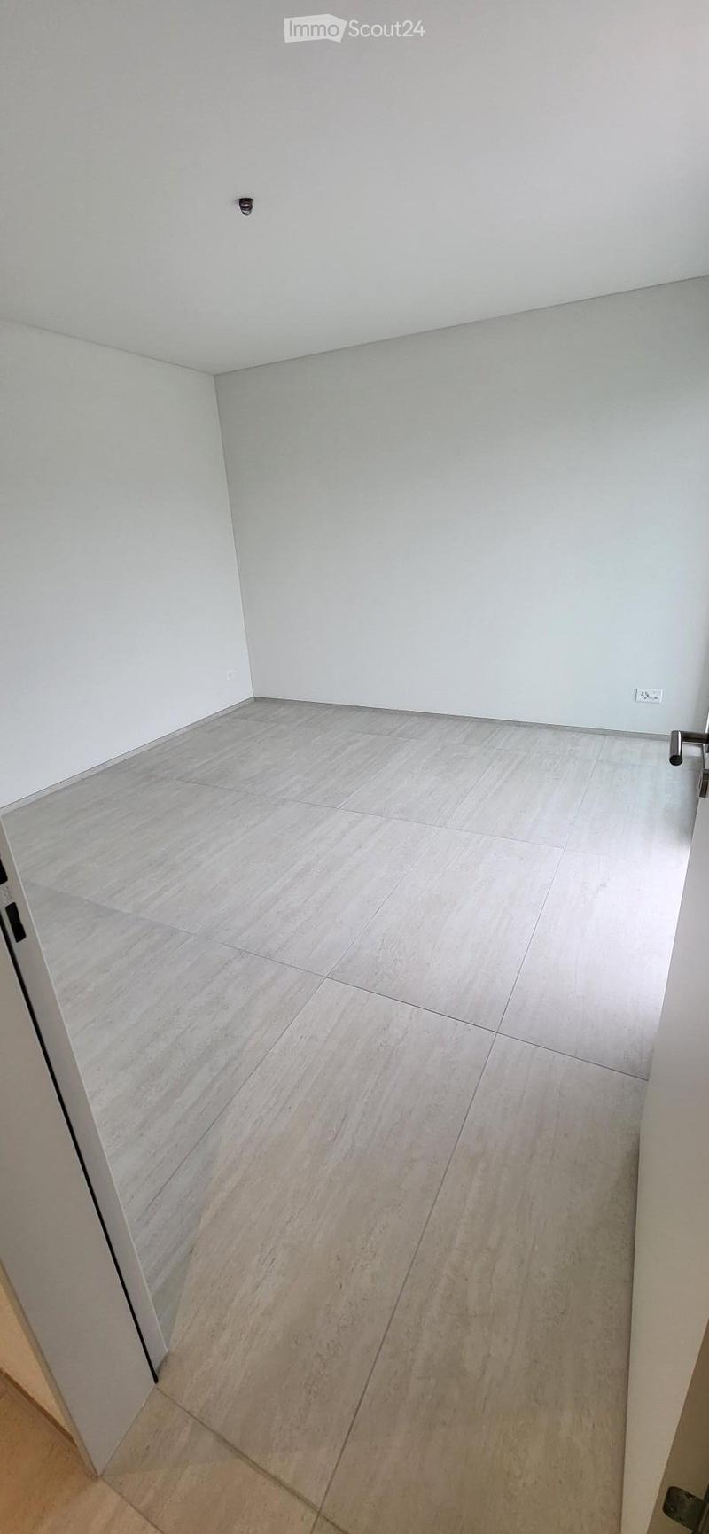 Empty room with white walls, tiled floor, and an open door.