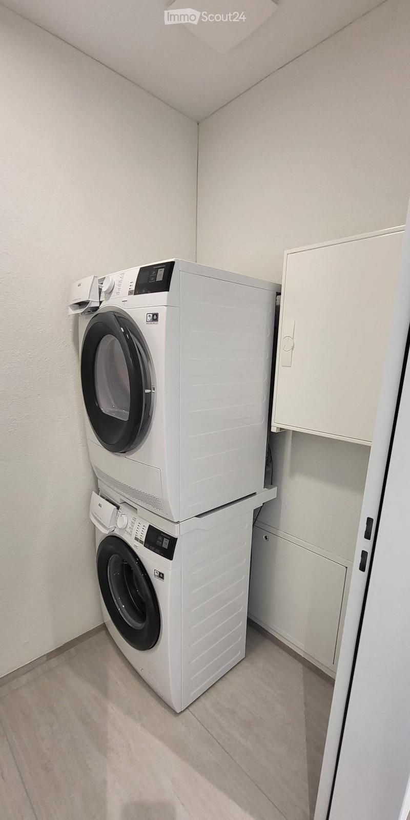 Laundry room with stacked washing machine and dryer, white cabinets, wooden floor