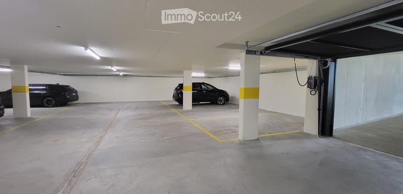 underground parking lot with two cars parked, yellow lines, white ceiling, white walls, pillars