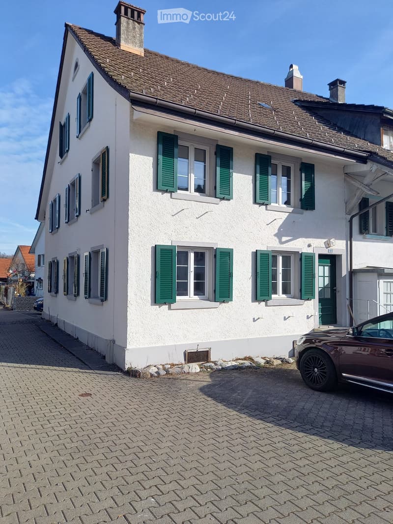 3 story house, white walls, green shutters, brown roof, brick driveway, car parked in front