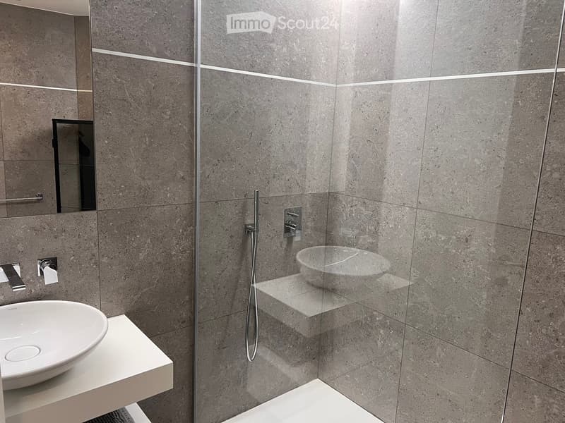 modern bathroom with gray tiles, a white sink, a glass shower enclosure, a silver faucet, and a mirror