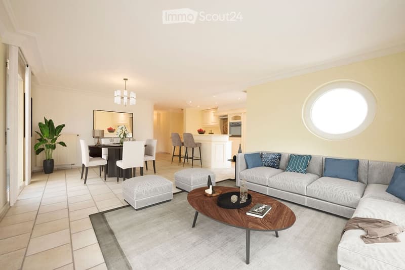 modern living room with gray sofa, wooden coffee table, round ottoman, dining table with chairs, potted plant, round window, kitchen with island