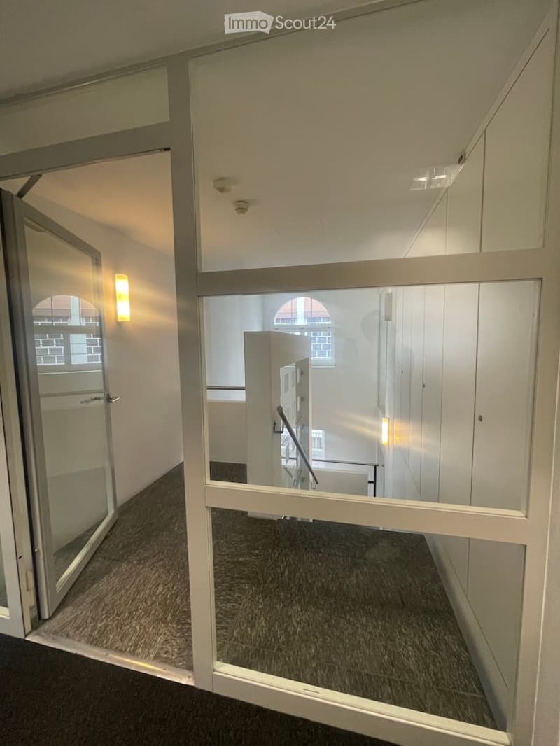 Empty room, glass door, glass wall, carpeted floor, white walls, ceiling lights, metal handrail