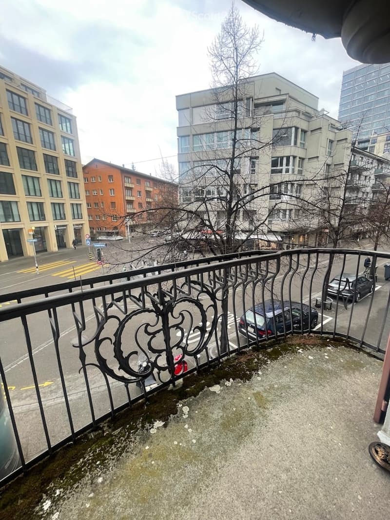 Balcony with railings, city street view, multiple buildings, cars parked on street