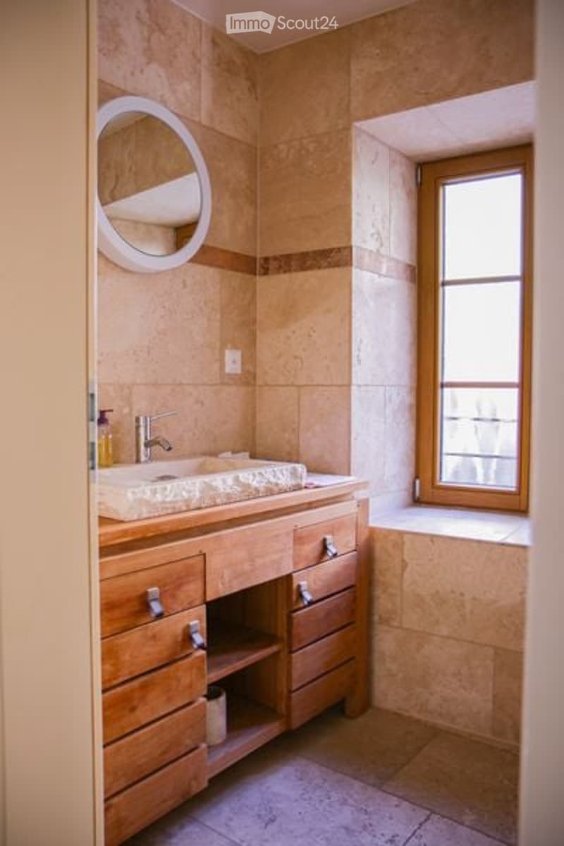 Bathroom with beige tiles, wooden cabinet, sink, mirror, window, and bathtub