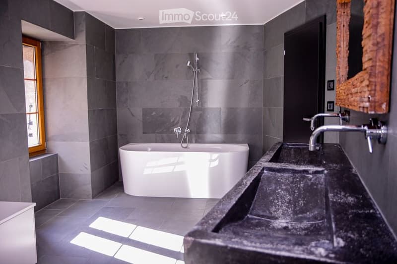 Bathroom with a bathtub, double sink, and gray tiled walls.