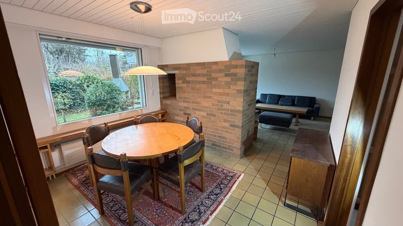 A round wooden table with chairs, a carpet, brick fireplace, and a window