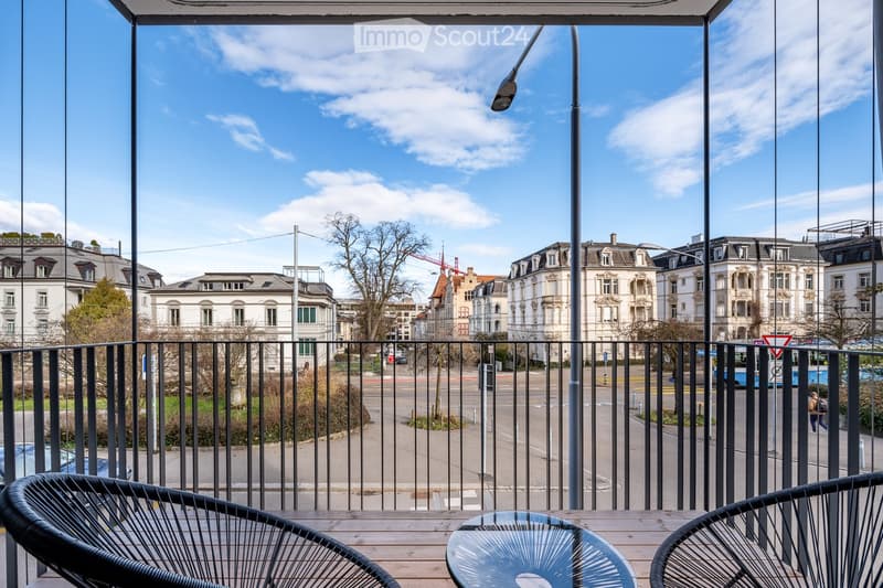 Balcony with a view of the city, two chairs, a table, and a black railing