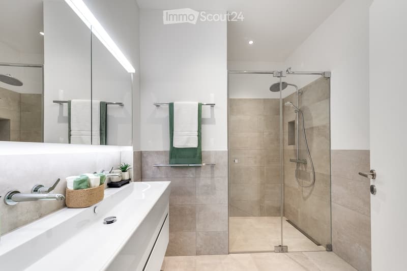 modern bathroom with white tiles, glass shower, white sink, towel racks, potted plant