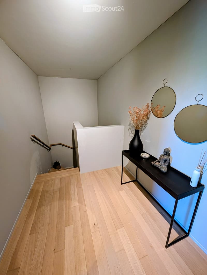 wooden floor, white walls, black table, vase, mirror, stairs