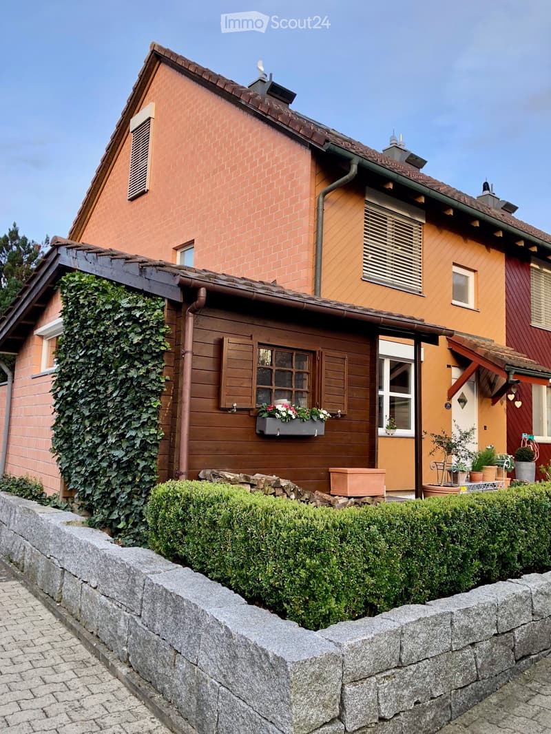 3 story house, brick walls, chimneys, brown roof, windows with shutters, outdoor plants, wall made of grey stones