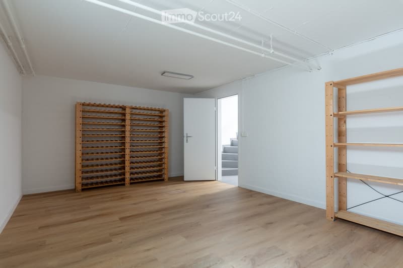 Empty room with wooden floor, white walls, wooden wine rack, open door, and wooden shelf.