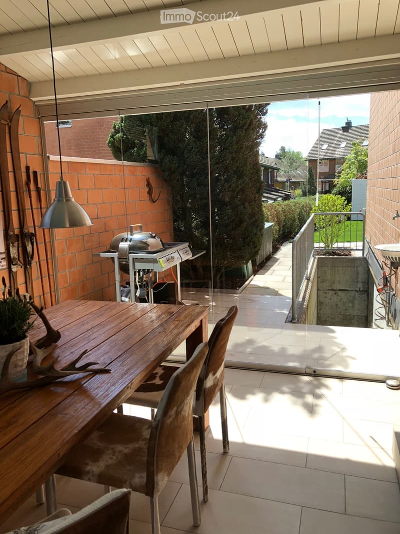 dining area with wooden table, chairs, brick wall, glass door, outdoor grill, potted plant, lamp