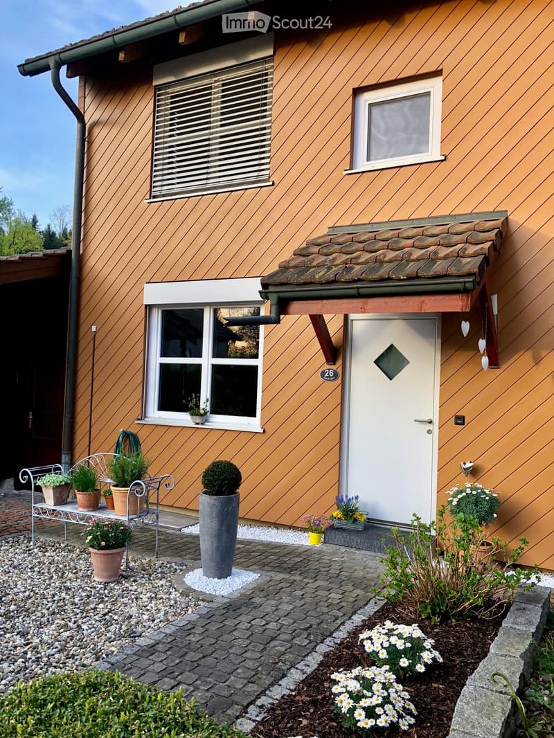 Cozy house, brown wooden panels, white windows, covered entrance, white gravel entrance, potted plants