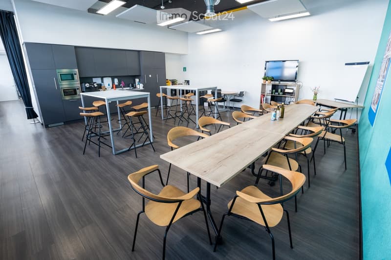 modern kitchen area with appliances, long tables, chairs, tv, whiteboard