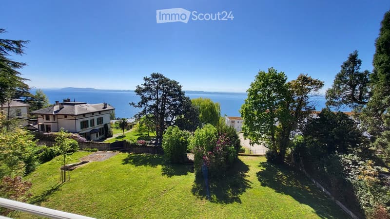 House with a view of the sea, surrounded by trees and plants, with a large lawn