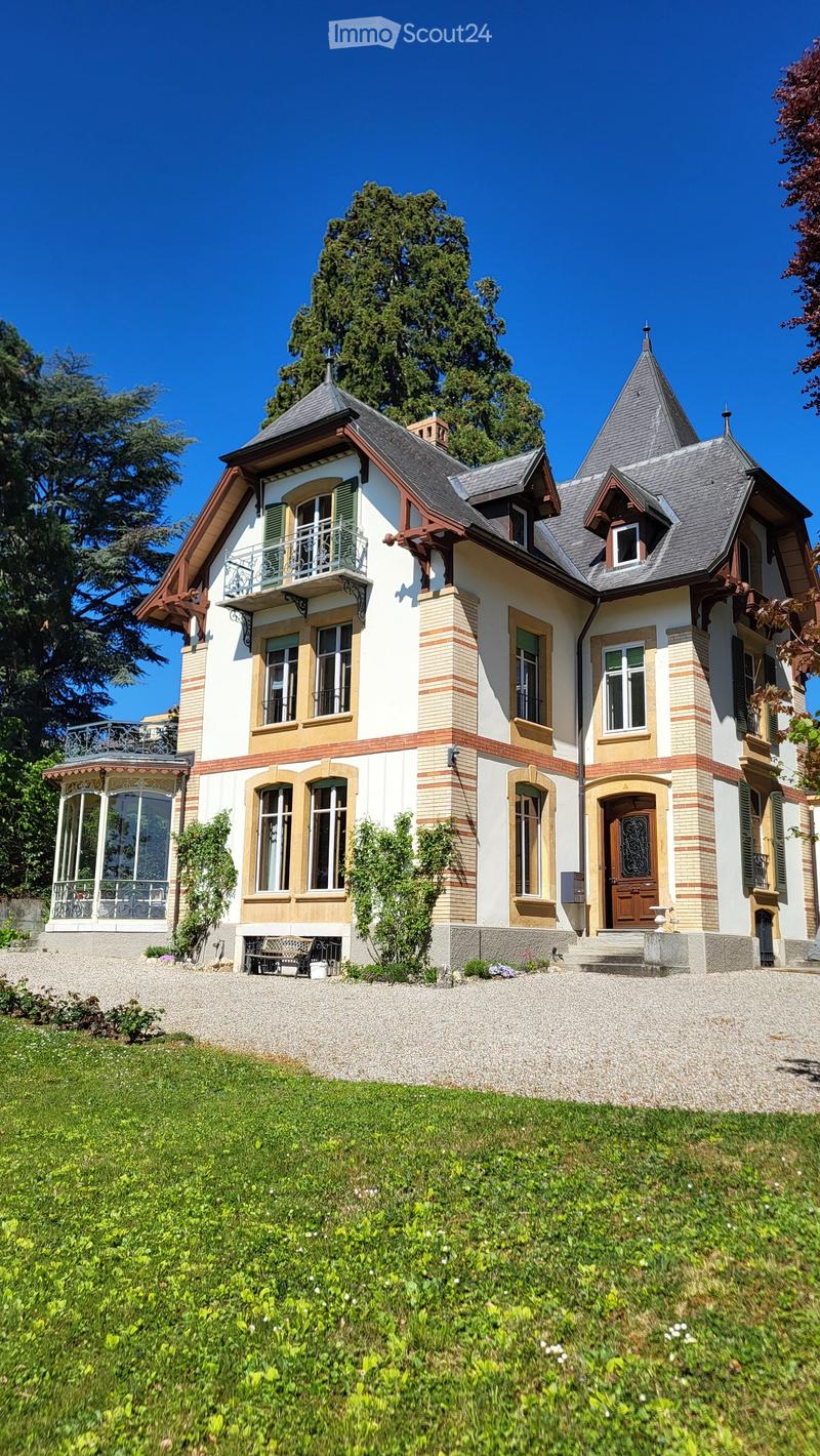 3 story house, white and brown exterior, large windows, balcony, gravel driveway, garden