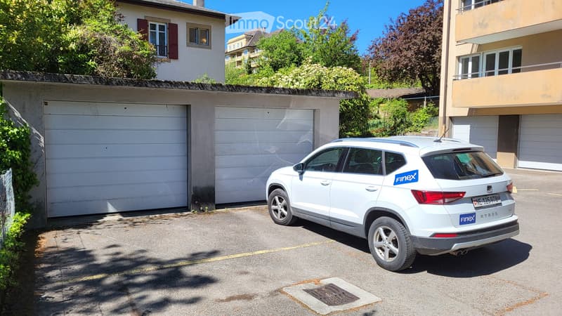 Two white garage doors, a white car parked in front, a building in the background