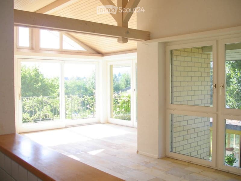 Empty room with wooden ceiling beams, tiled floor, and large glass doors leading to a balcony.