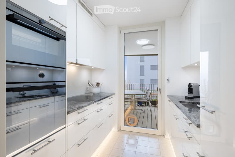 modern kitchen with a double oven, granite countertops, stainless steel appliances, white cabinetry, open sliding door leading to a balcony with an outdoor table and chairs
