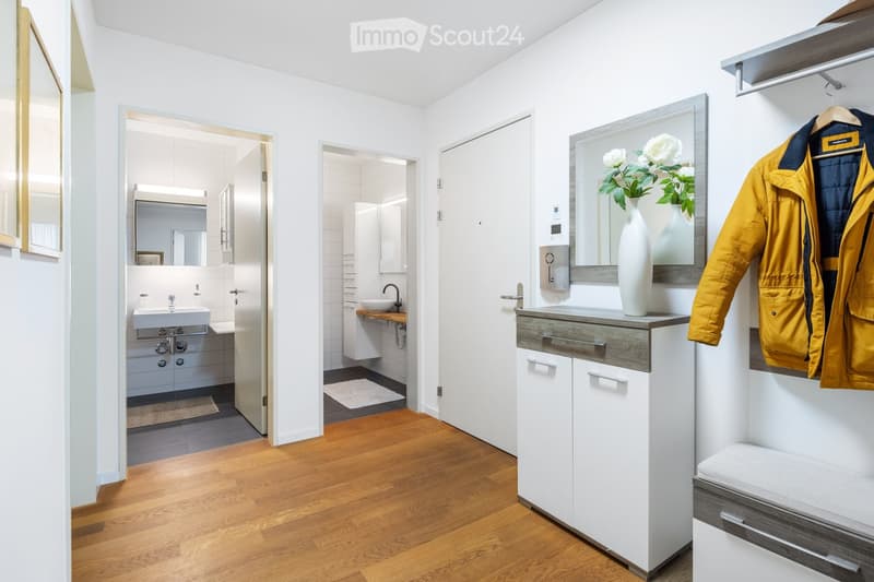 Entrance hallway with a closet and mirror, leading to a bathroom with sink and a small bedroom with a built-in wardrobe and a sink.