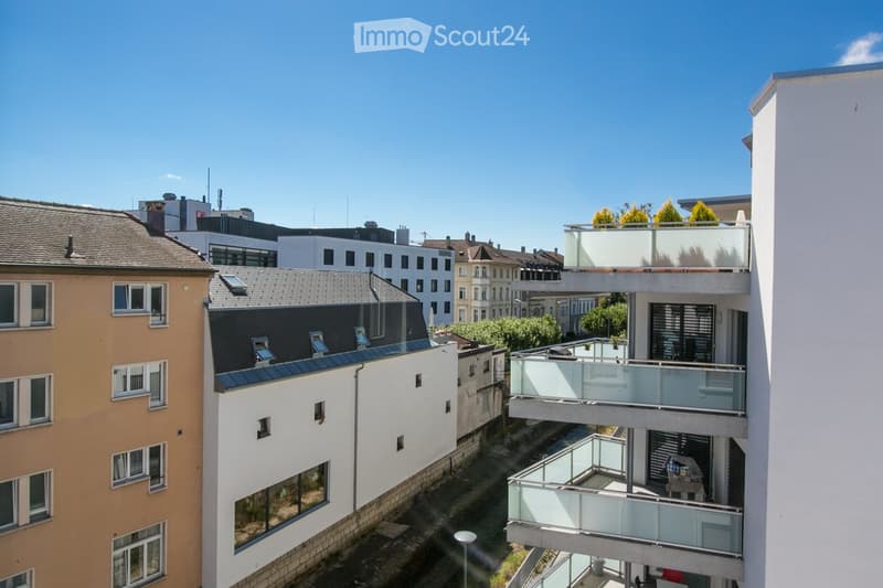Aerial view of a building with multiple balconies, surrounded by other buildings and greenery.