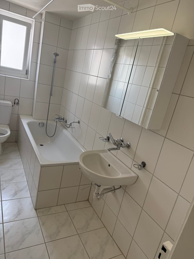 Bathroom with white tiles, bathtub, toilet, sink, and mirror.