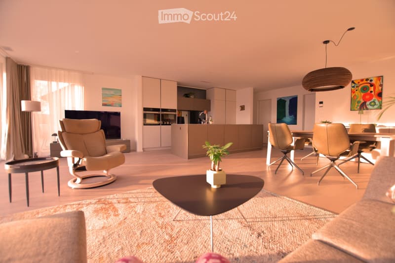open plan living room with kitchen, beige furniture, wooden floor, large windows, dining table, TV, artwork
