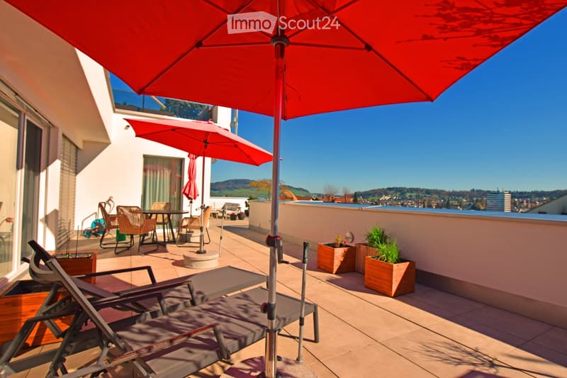 Terrace with lounge chairs, tables, chairs, and umbrellas, with a view of the city