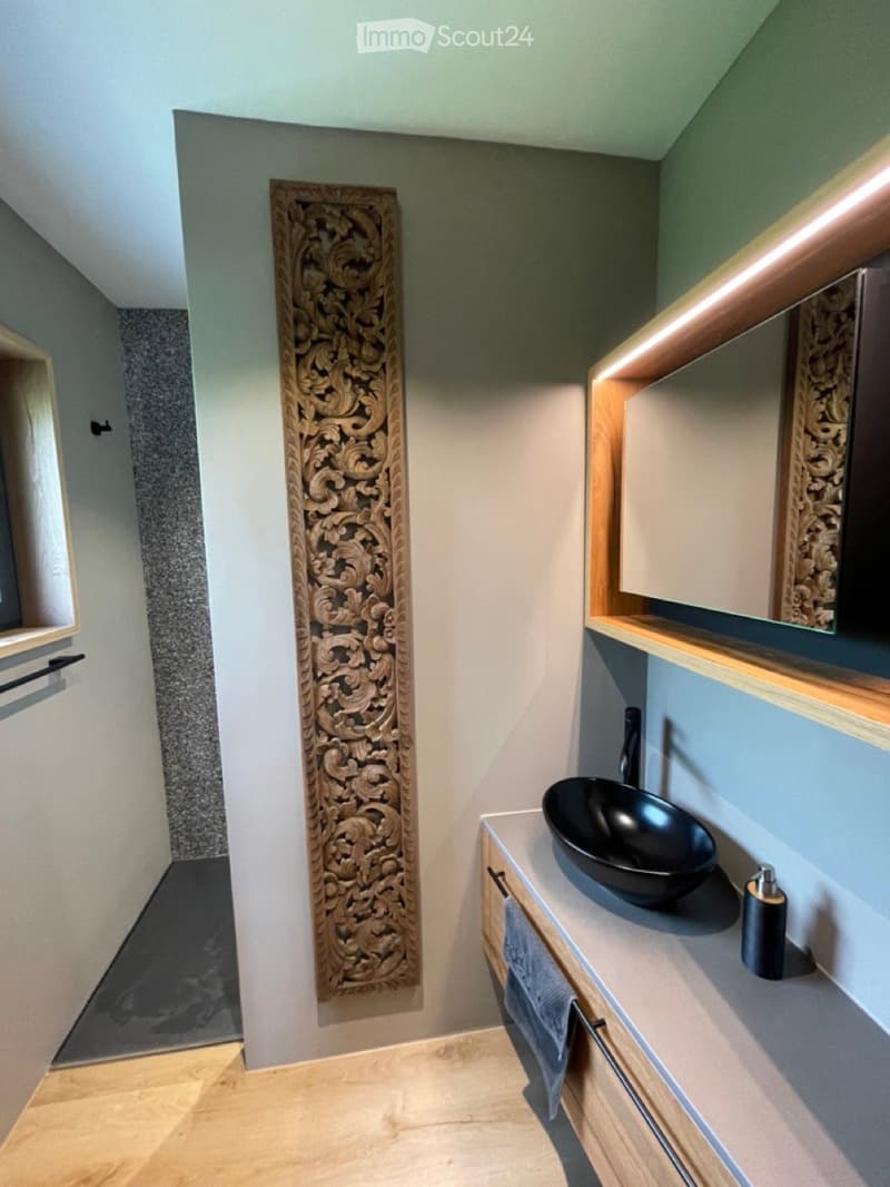 Bathroom with walk-in shower, black sink, carved wood wall panel, mirror, wooden cabinet