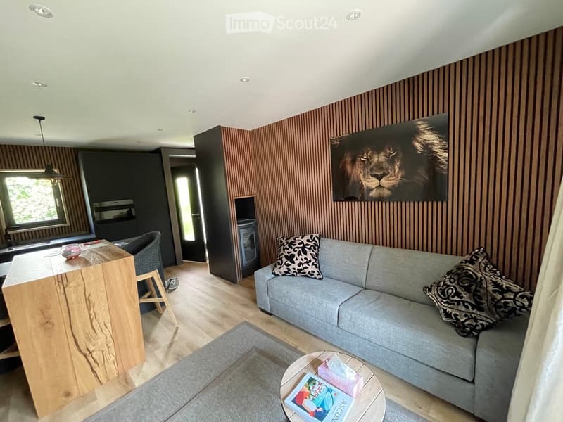 wooden flooring, wooden kitchen counter, gray sofa, wooden coffee table, rug, picture frame on wall, chair, wooden cabinet, desk, hanging lamp, fireplace